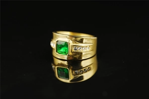 Macro detail of men's gold titanium ring with emerald-cut green stone and side diamonds