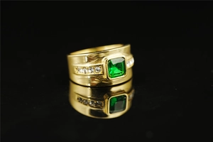 Macro shot of gold-plated titanium ring with emerald green stone and side diamonds