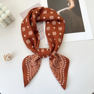Close-up of caramel paisley silk scarf tied in a bow with minimalist props and accessories