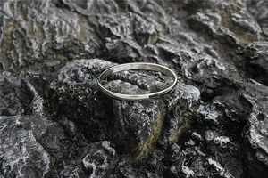 Close-up of minimalist silver titanium steel bangle on textured black volcanic rock background