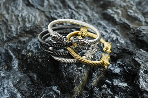 Detalle de las pulseras de cable con cabeza de dragón en oro, plata y negro sobre roca volcánica