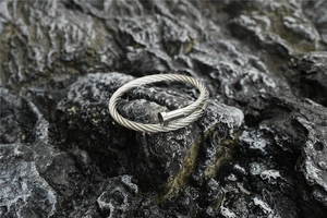Macro shot of silver twisted cable cuff bracelet resting on a dark textured rock