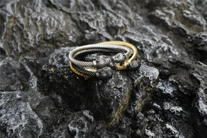 Detailed close-up of double leopard head twist bangle with green gemstone eyes on dark rock