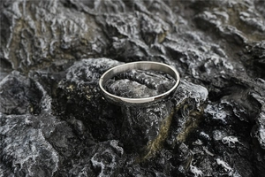 Close-up of polished silver titanium steel bangle on a dark natural rock background