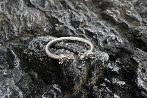 Detalle de brazalete de cable con cabeza de dragón plateada sobre fondo de roca oscura