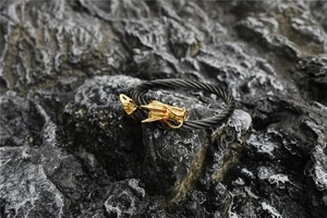 Close-up of golden dragon head with red stone eyes on a black cable cuff bracelet