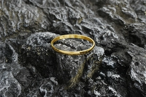 Detailed close-up of a minimalist gold-plated steel bangle with mirror finish and hinge clasp