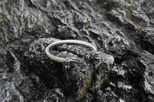 Detalle de cabezas de dragón vikingo en brazalete de acero trenzado sobre piedra negra