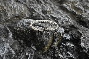 Close-up of a braided stainless steel Viking lion head bracelet on a natural black rock