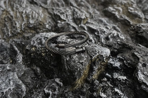 Detail of a black steel cable nail bracelet on a textured dark rock background