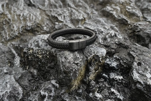 Gros plan du bracelet en cuir tressé noir avec fermoir magnétique mat sur roche volcanique