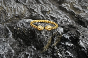 Detailed view of gold Viking lion head bracelet with intricate woven metal texture on rock