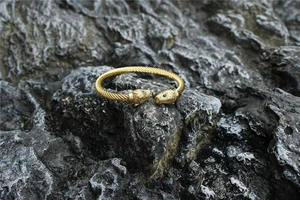 Detail of twisted gold bangle with leopard heads and green stone eyes on dark rock