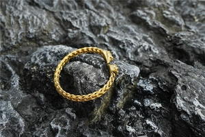 Detailed close-up of woven gold lion head cuff bracelet on a natural stone surface