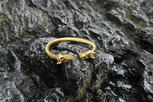 Vista detallada de una pulsera dorada de cabeza de dragón trenzada sobre roca oscura