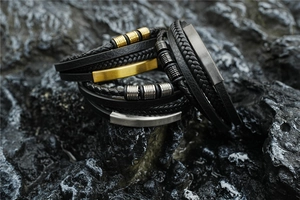 Detail of multi-layer woven black leather bracelets with metallic accents on dark rock