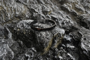 Polished black titanium steel minimalist bangle on a textured grey stone surface
