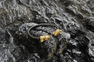 Detalle de cabezas de dragón doradas en un brazalete de cable trenzado negro