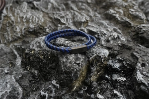 Detail of blue and black braided double-wrap bracelet with magnetic metal clasp on rock