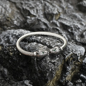 Twisted steel bangle featuring dual leopard heads with green zircon eyes on a rock background