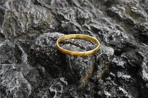 Close-up of a minimalist golden titanium steel open bangle on a dark grey rock surface