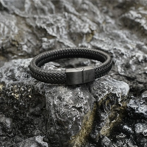 Bracelet tressé en cuir noir avec fermoir magnétique en acier mat sur fond de roche