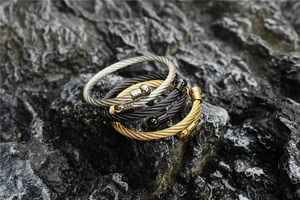 Macro detail of twisted cable bangles in gold, silver and black on a natural stone surface