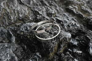 Detailed view of two polished silver stainless steel oval bangles on dark rock background