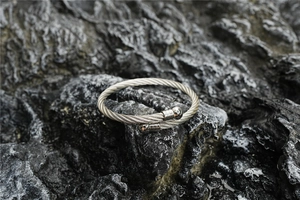 Detail of silver stainless steel twisted cable bracelet on a textured dark rock background