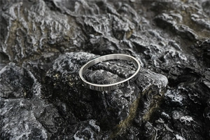 Detailed close-up of polished silver steel oval bangle with hinge on dark volcanic stone