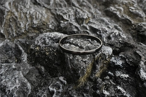 Detail shot of matte black stainless steel bangle on a textured grey stone surface