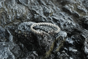 Detailed view of silver braided wolf head bangle on dark volcanic rock background