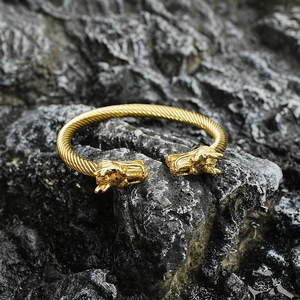 Brazalete trenzado dorado con cabezas de dragón sobre fondo de piedra oscura