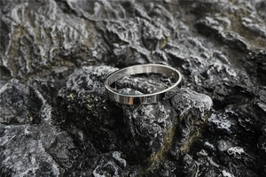 Close-up of silver minimalist bangle with mirror finish on a dark volcanic rock
