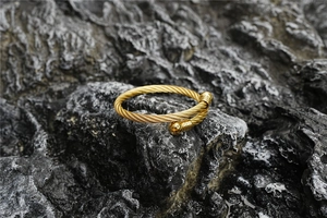 Detailed view of golden twisted cable bangle with round end beads on a textured stone