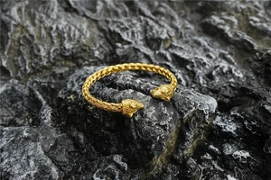 Close-up of golden wolf head bangle with intricate braided texture on a dark rock