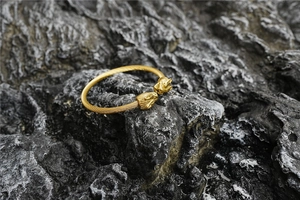 Détail de têtes de lion dorées sur un bracelet jonc ouvert en câble d'acier torsadé