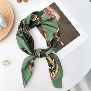 Detailed view of luxury green silk scarf with gold chain patterns on a stylish table