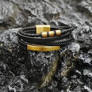 Multilayer black woven leather bracelet with gold magnetic clasp on a dark rock background
