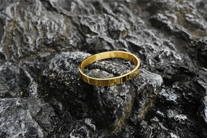 Polished gold oval bangle featuring a minimalist hinge closure on dark textured rock