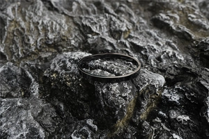 Polished black stainless steel oval bangle on a textured dark volcanic rock background