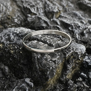 Minimalist silver titanium steel bangle with polished mirror finish on stone background