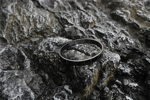 Detail view of a matte black titanium steel oval bracelet on dark textured volcanic rock