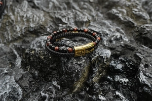 Close-up of tiger eye stone beads and braided leather cord on a rough rock surface