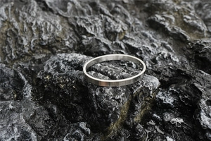 Detailed close-up of brushed silver stainless steel oval bangle on dark rock texture