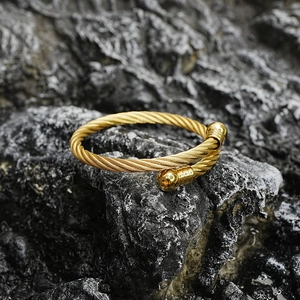 Polished gold twisted cable stainless steel cuff bracelet on a dark stone background