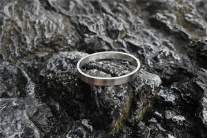 Detailed close-up of brushed silver stainless steel oval bangle on black volcanic rock