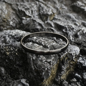 Minimalist matte dark grey titanium steel bangle shown on a textured rock surface
