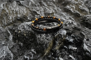 Détail de perles œil de tigre et bracelet en cuir tressé noir sur pierre sombre humide