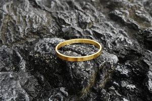 Detailed macro view of gold brushed oval bangle on a dark grey rock background